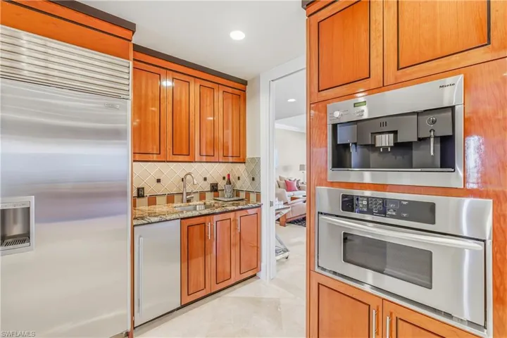 Kitchen featuring stainless steel appliances, light stone countertops, recessed lighting, brown cabinetry, and tasteful backsplash