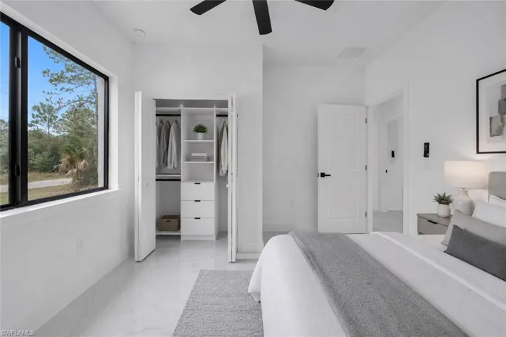 Bedroom featuring a large rectangular window with black trim, a built-in closet system with drawers and shelving, white walls, and light-colored tile flooring