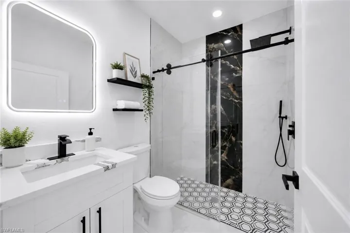 Bathroom featuring a white vanity with a stone-finish countertop, black faucet, and an illuminated mirror