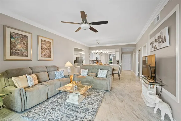 Living room featuring ceiling fan with notable chandelier and crown molding