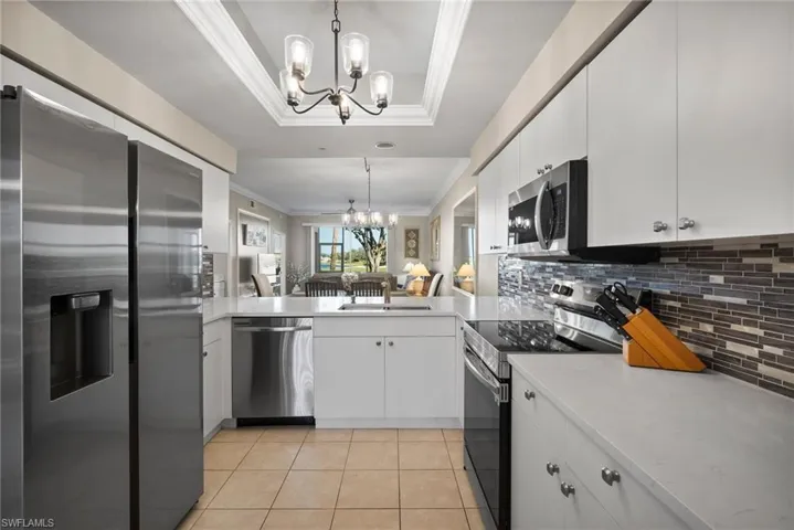Kitchen featuring hanging light fixtures, an inviting chandelier, a tray ceiling, white cabinets, and appliances with stainless steel finishes
