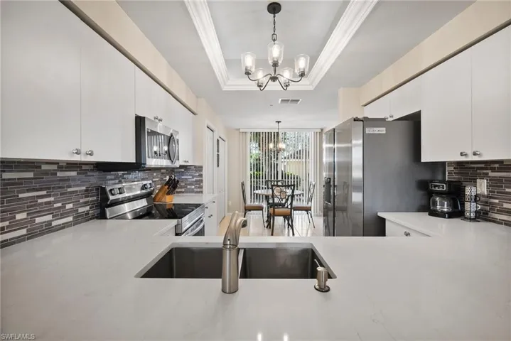 Kitchen with a raised ceiling, sink, hanging light fixtures, and appliances with stainless steel finishes