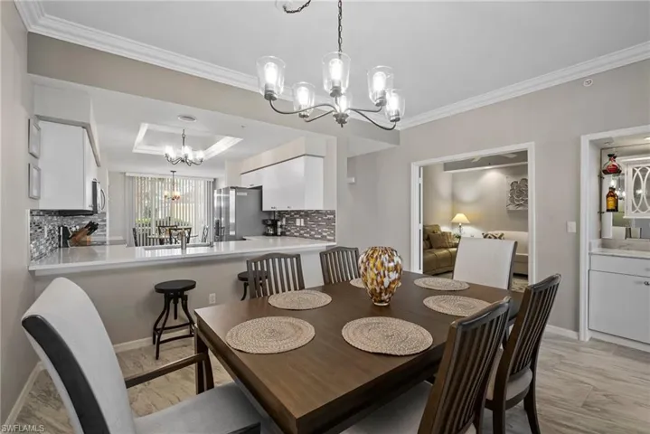 Dining space with sink, a raised ceiling, a notable chandelier, and crown molding