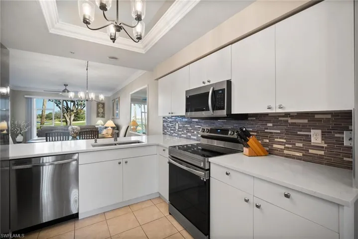 Kitchen featuring backsplash, stainless steel appliances, a raised ceiling, pendant lighting, and white cabinets