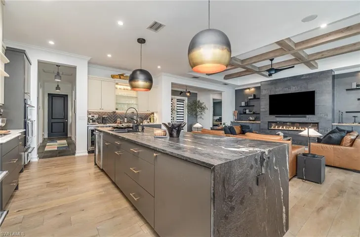 Kitchen with light wood-type flooring, hanging light fixtures, a spacious island, and sink