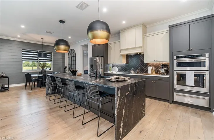 Kitchen with dark stone counters, a kitchen island with sink, white cabinetry, hanging light fixtures, and stainless steel appliances