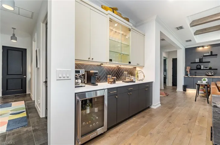 Bar featuring white cabinetry, wine cooler, backsplash, light wood-type flooring, and ornamental molding