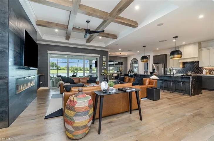 Living room with coffered ceiling, beamed ceiling, a large fireplace, light hardwood / wood-style flooring, and ceiling fan