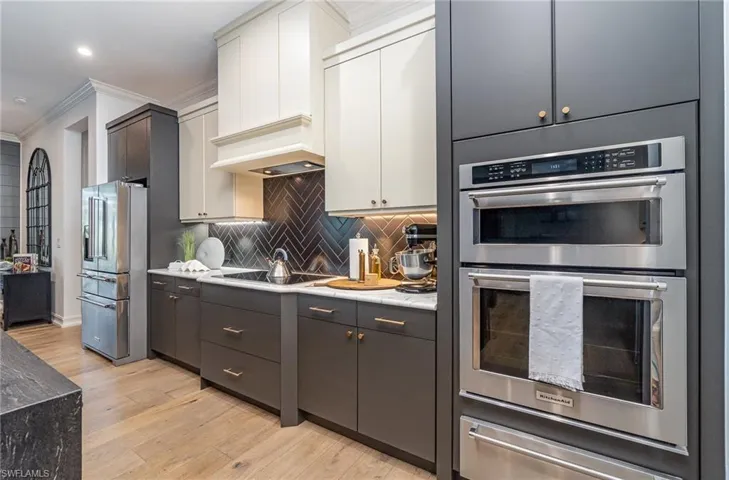Kitchen with white cabinetry, appliances with stainless steel finishes, crown molding, light hardwood / wood-style floors, and decorative backsplash