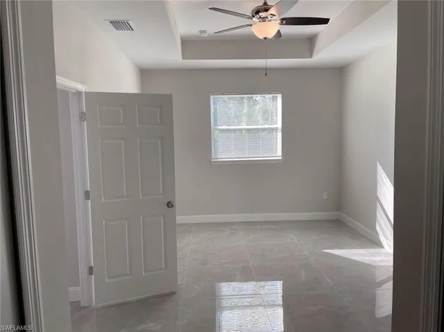 Unfurnished room featuring a raised ceiling, ceiling fan, and light tile floors