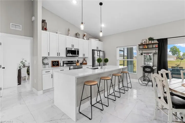 Kitchen with pendant lighting, appliances with stainless steel finishes, white cabinetry, light stone counters, and a breakfast bar area