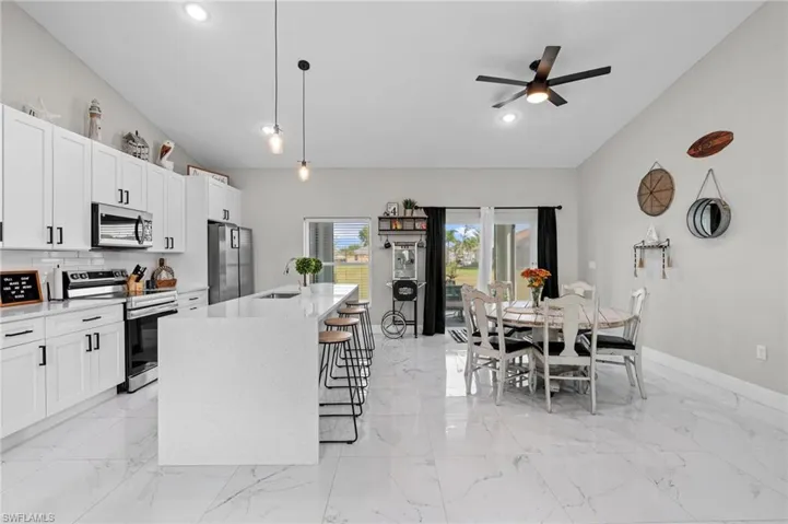 Kitchen featuring stainless steel appliances, hanging light fixtures, light stone countertops, a center island with sink, and white cabinetry