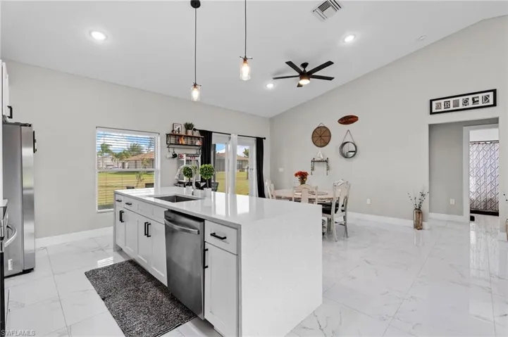 Kitchen featuring white cabinetry, lofted ceiling, pendant lighting, light stone counters, and stainless steel appliances