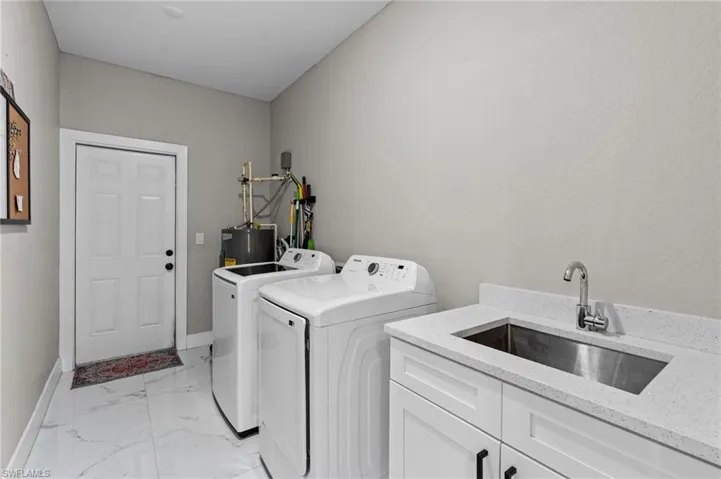 Laundry area featuring light marble finish flooring, washing machine and dryer, electric water heater, and cabinet space