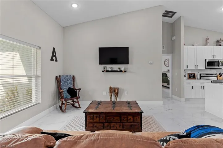 Living area featuring vaulted ceiling, recessed lighting, and light marble finish flooring