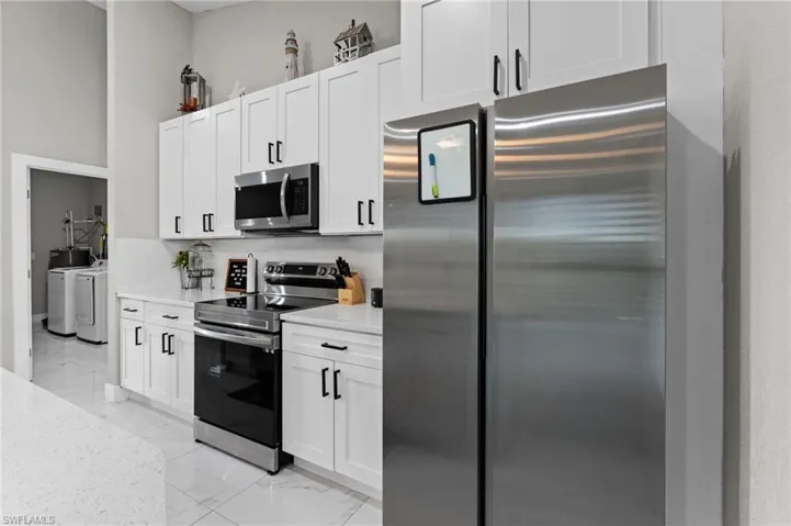 Kitchen with stainless steel appliances, separate washer and dryer, light stone counters, light marble finish flooring, and white cabinets