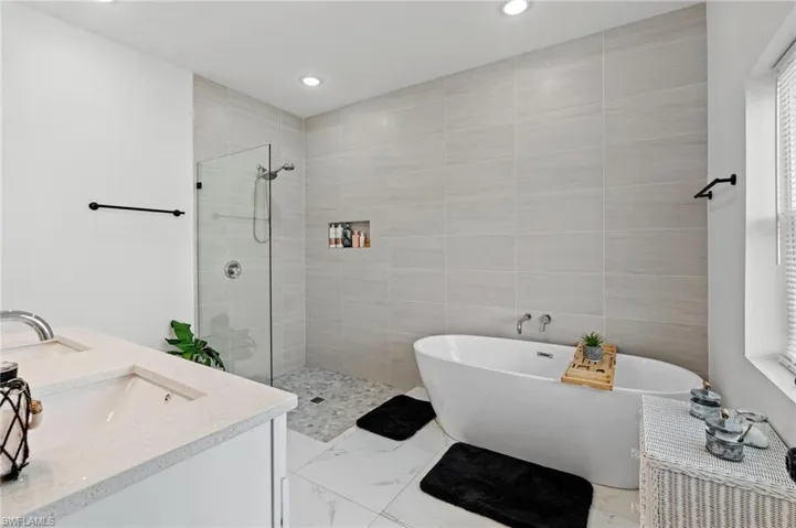 Bathroom featuring a freestanding tub, double vanity, walk in shower, light marble finish flooring, and recessed lighting