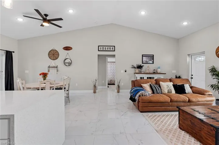 Living room featuring vaulted ceiling, recessed lighting, light marble finish floors, and a ceiling fan