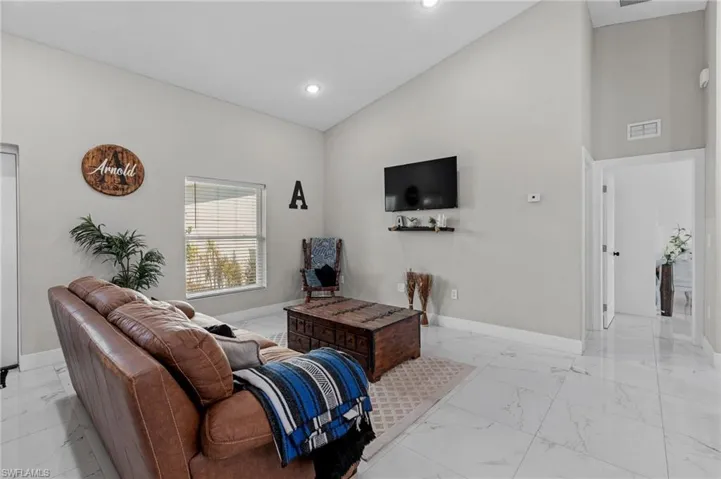 Living room featuring high vaulted ceiling, light marble finish floors, and recessed lighting