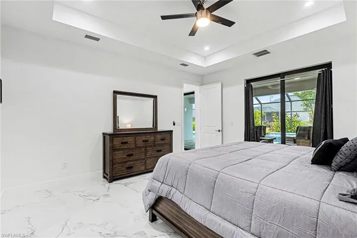 Bedroom with a tray ceiling, access to outside, a ceiling fan, recessed lighting, and light marble finish floors