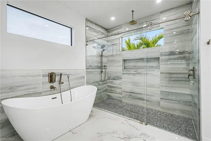 Bathroom with tile walls, a soaking tub, healthy amount of natural light, a stall shower, and a wainscoted wall