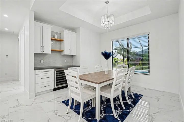 Dining space with beverage cooler, a chandelier, light marble finish flooring, and a raised ceiling