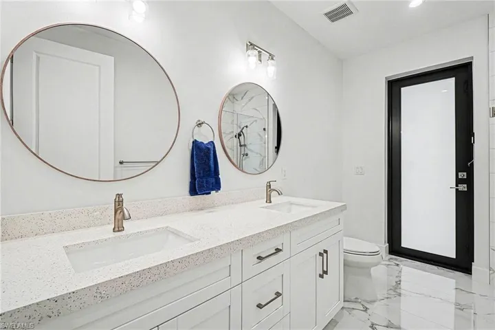 Full bathroom with double vanity, light marble finish flooring, and an enclosed shower