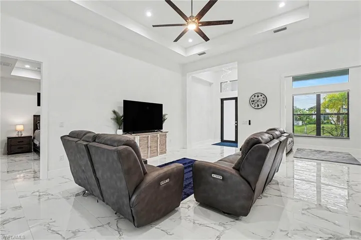 Living area with ceiling fan, recessed lighting, light marble finish floors, and a tray ceiling