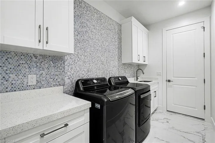 Laundry area with cabinet space, light marble finish floors, and washing machine and dryer