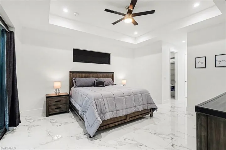 Bedroom featuring a tray ceiling, ceiling fan, light marble finish floors, recessed lighting, and a spacious closet