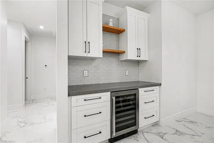 Bar area featuring white cabinets, beverage cooler, open shelves, backsplash, and dark stone counters