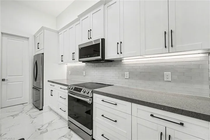 Kitchen with stainless steel appliances, dark countertops, white cabinets, and light marble finish flooring