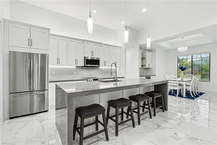 Kitchen featuring stainless steel appliances, light stone counters, white cabinets, a center island with sink, and open shelves
