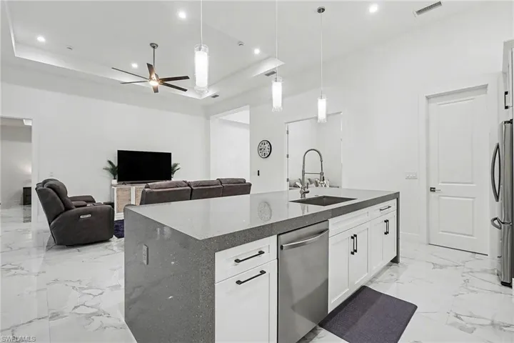 Kitchen featuring a kitchen island with sink, dark stone countertops, stainless steel appliances, open floor plan, and decorative light fixtures
