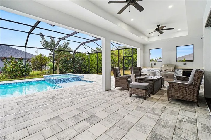 Relaxing pool / spa featuring an outdoor kitchen and area to lounge, a patio, a sunroom, and a lanai
