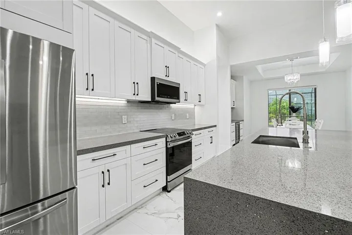 Kitchen featuring stainless steel appliances, white cabinetry, dark stone counters, tasteful backsplash, and a tray ceiling