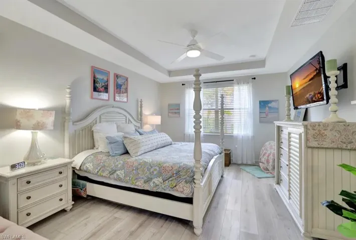 Bedroom featuring a raised ceiling, wood-style flooring, and a ceiling fan