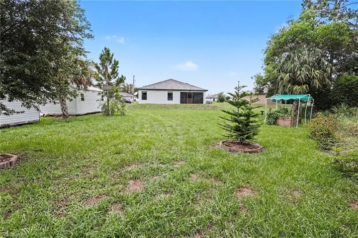 Expansive rear yard featuring a lawn, mature trees, and a distant single-story structure with a screened patio