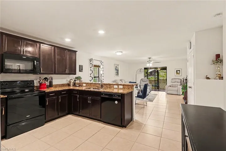 Kitchen featuring dark wood cabinetry, black appliances, and granite-style countertops