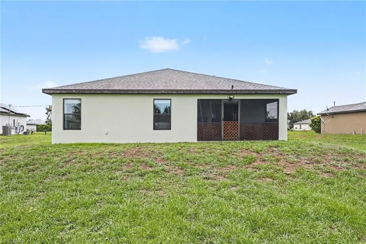 Rear exterior featuring a screened-in patio, white stucco siding, and a shingle roof