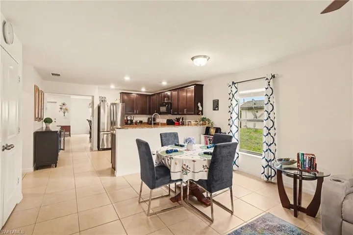 Open-concept living space featuring neutral tile flooring, a kitchen with dark wood cabinetry, stainless steel appliances, and a breakfast bar