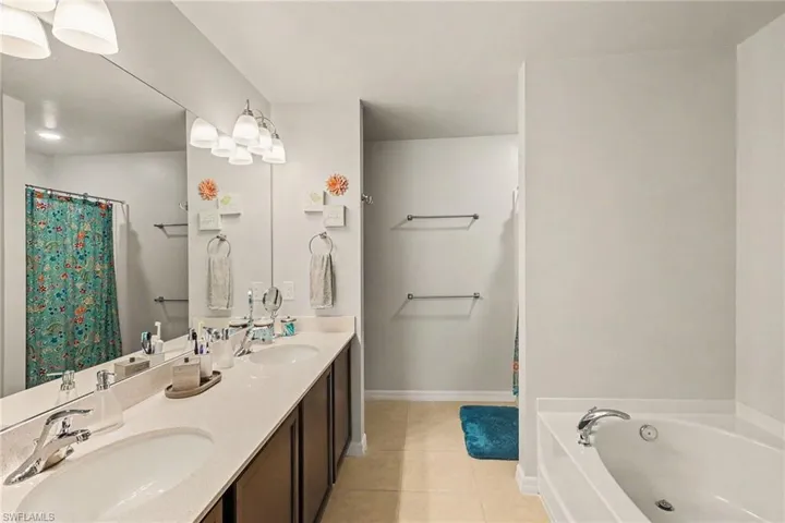 Bathroom featuring a dual vanity with undermount sinks and a light-toned countertop, a soaking tub, and a separate shower area