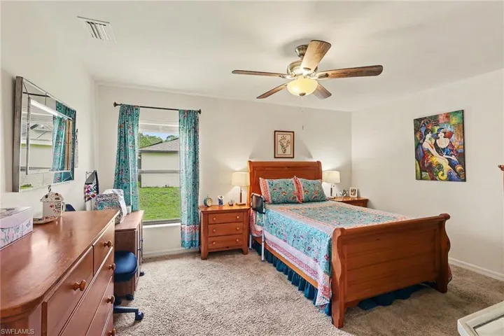 Carpeted bedroom featuring a ceiling fan with integrated lighting, a window with a green exterior, and white painted walls