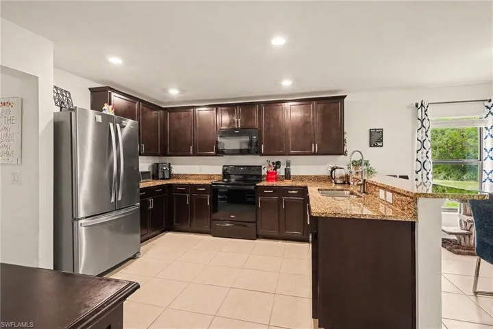 Kitchen featuring dark wood cabinetry, granite countertops, stainless steel refrigerator, black range, and recessed lighting