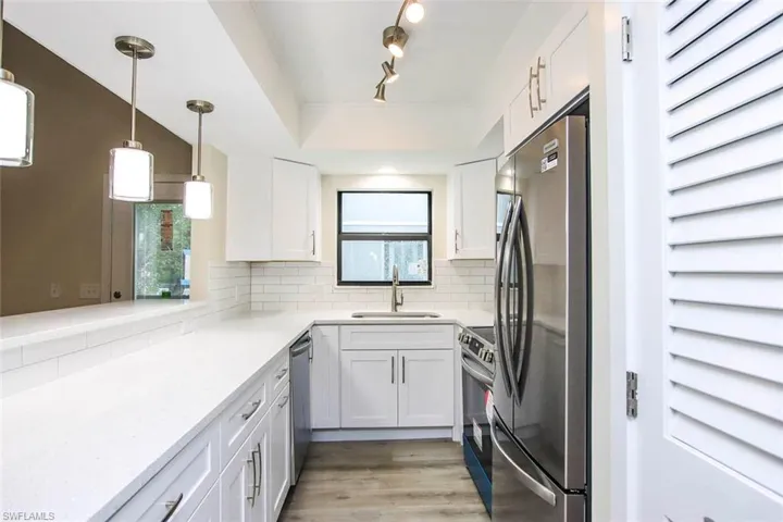 Kitchen featuring decorative light fixtures, light hardwood / wood-style floors, stainless steel appliances, tasteful backsplash, and sink