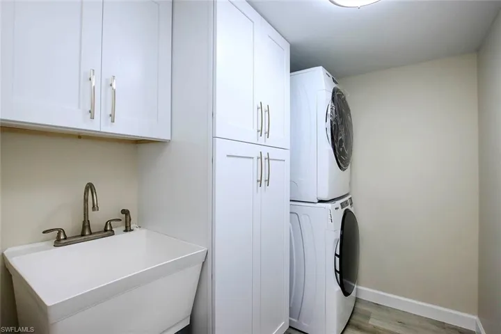 Laundry area with stacked washer and clothes dryer, sink, light hardwood / wood-style floors, and cabinets
