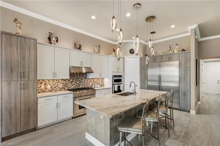 Kitchen featuring under cabinet range hood, white cabinetry, hanging light fixtures, high end appliances, and a center island with sink