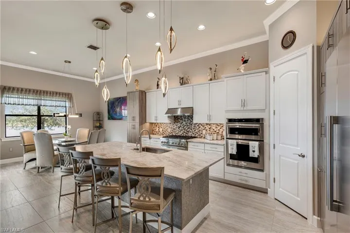 Kitchen with a center island with sink, hanging light fixtures, under cabinet range hood, white cabinetry, and a sink