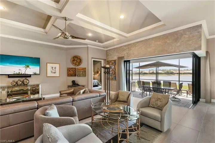 Living room featuring baseboards, coffered ceiling, a ceiling fan, ornamental molding, and a water view