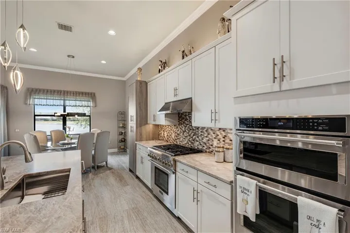 Kitchen featuring decorative light fixtures, stainless steel appliances, white cabinets, a sink, and under cabinet range hood